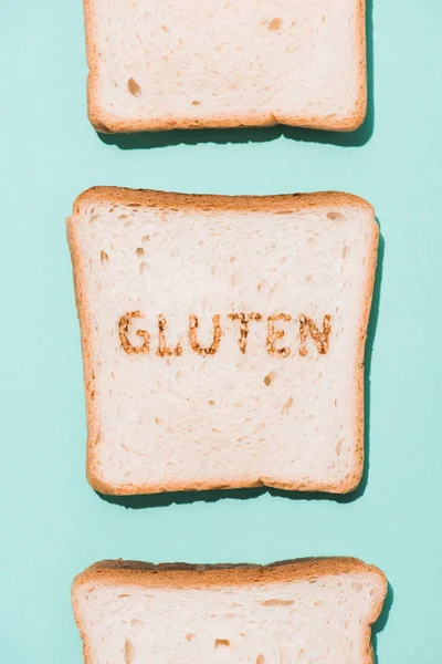 Vista superior de la fila de rebanadas de pan con signo de gluten en la superficie azul - foto de stock