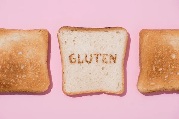 Top view of row of toasts and slice of bread with burned gluten sign on pink surface — Stock Photo