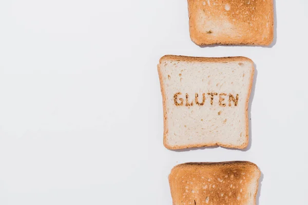Top view of row of toasts and slice of bread with burned gluten sign on white surface — Stock Photo