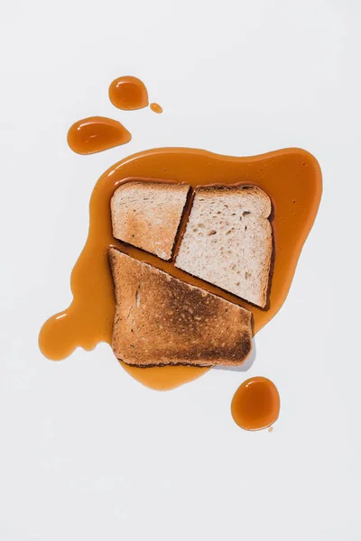 Vue du dessus d'une tranche de pain avec des morceaux rôtis sur du sirop brun renversé sur une surface blanche — Photo de stock