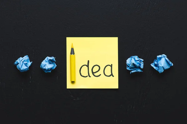 'idea' palabra escrita en nota adhesiva y bolas de papel arrugado azul sobre fondo negro, concepto de ideas - foto de stock