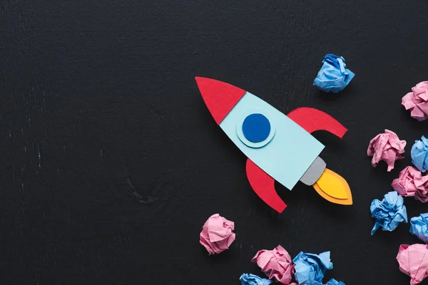 Cardboard rocket with crumpled paper balls and copy space on black background, setting goals concept — Stock Photo