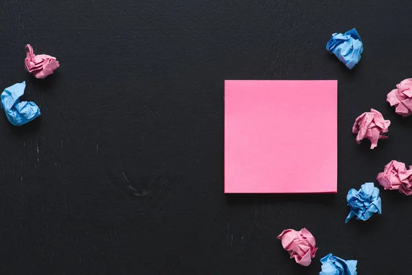 Vue du dessus de boules de papier froissées dispersées roses et bleues avec une note collante sur fond noir, pensez à un concept différent — Photo de stock