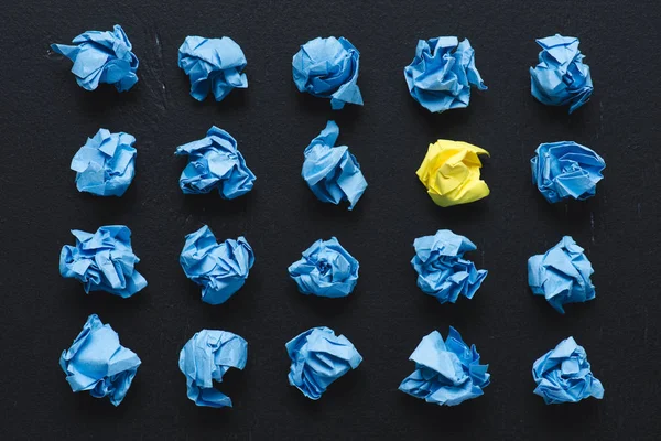 Top view of blue crumpled paper balls with yellow one on black background, think different concept — Stock Photo