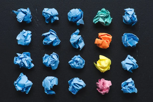 Top view of crumpled paper balls with row of colorful ones on black background, think different concept — Stock Photo