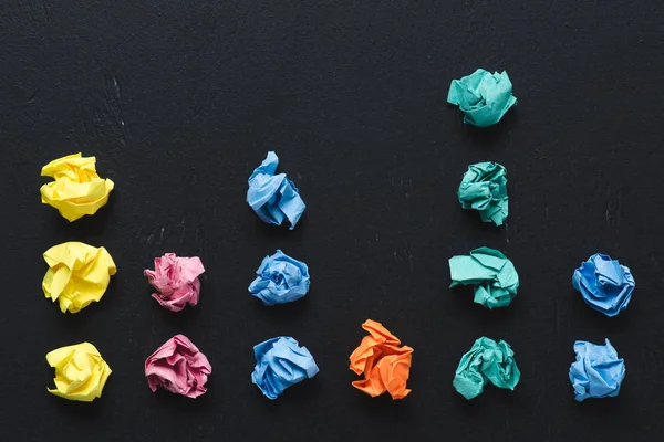 Vue de dessus des boules de papier froissées colorées disposées sur fond noir, penser concept différent — Photo de stock