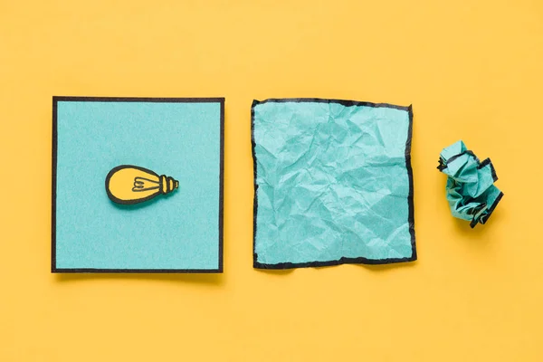 Top view of note with light bulb drawing and crumpled paper on yellow background, ideas concept — Stock Photo