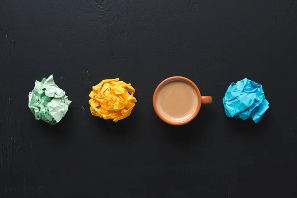 Draufsicht auf bunte zerknüllte Papierkugeln mit Kaffeetasse auf schwarzem Hintergrund — Stockfoto