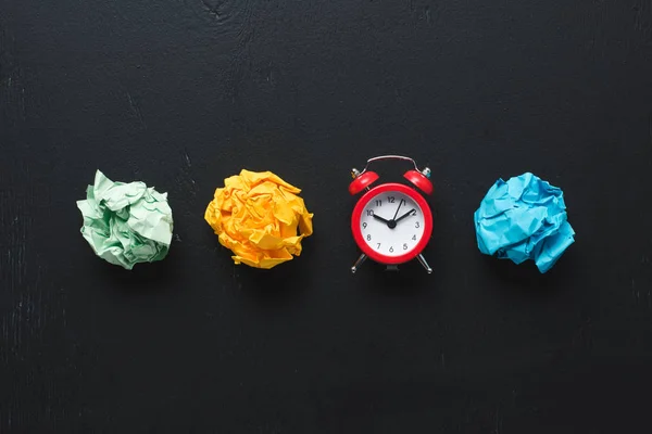 Vista superior de coloridas bolas de papel arrugado y reloj sobre fondo negro, concepto de gestión del tiempo - foto de stock