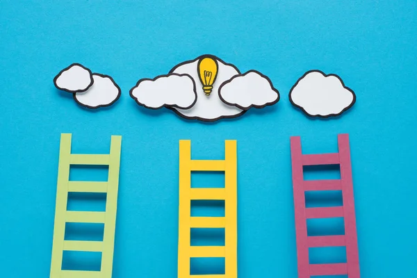 Vista superior de escaleras de cartón con bombilla y nubes sobre fondo azul, concepto de ideas - foto de stock