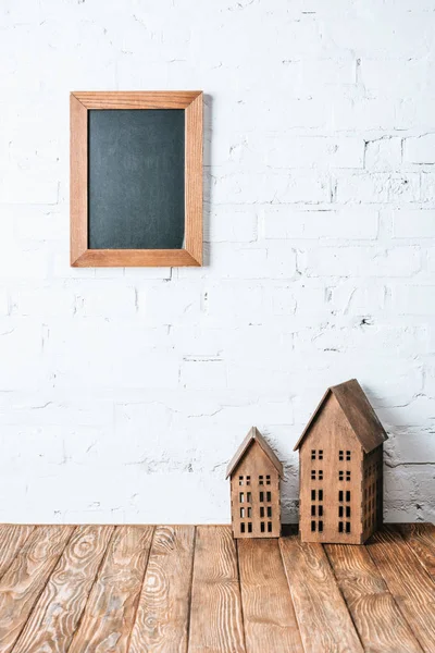 Quadro em branco marrom na parede de tijolo branco com modelos de casa rústica na mesa de madeira — Fotografia de Stock