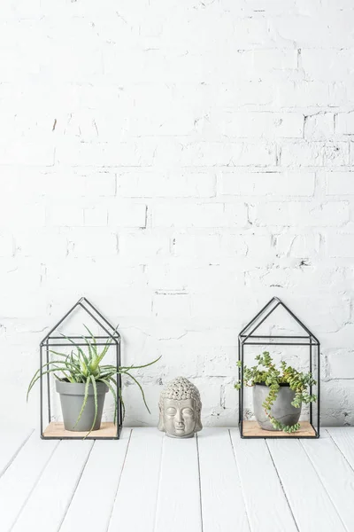 Plantas verdes en macetas y figura de cerámica buddha en mesa de madera cerca de la pared de ladrillo blanco - foto de stock