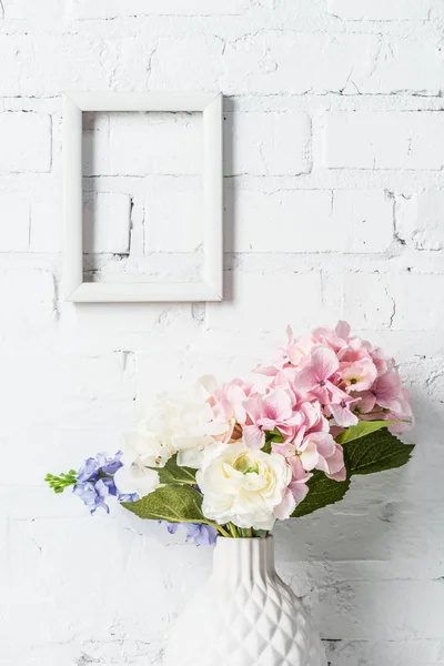 Weißer leerer Rahmen auf Ziegelwand mit Blumen in Keramikvase — Stockfoto
