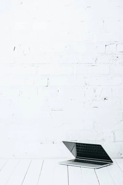 Ноутбук на белом деревянном столе возле кирпичной стены — стоковое фото