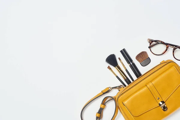 Óculos, rímel, escovas cosméticas e saco amarelo sobre fundo branco — Fotografia de Stock