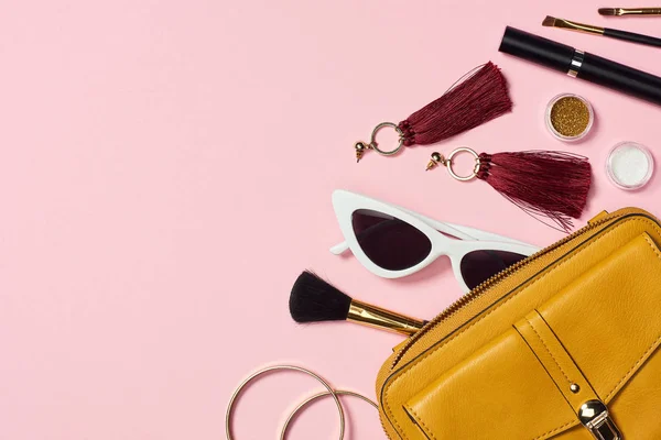 Draufsicht auf Armbänder, Ohrringe, Sonnenbrille, Wimperntusche, Kosmetikbürsten, Lidschatten und Tasche auf rosa Hintergrund — Stockfoto
