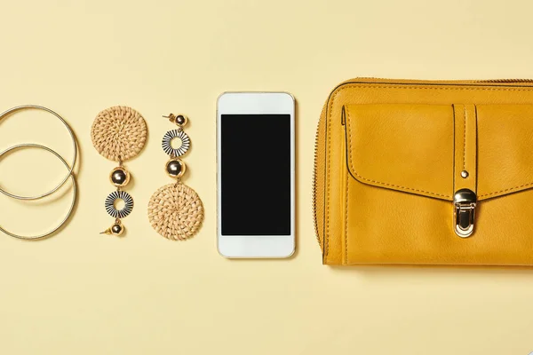 Vista superior de pulseras, pendientes, smartphone y bolso sobre fondo amarillo - foto de stock