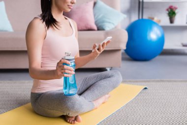 yoga mat egzersiz yaptıktan sonra rahatlatıcı ve smartphone kullanarak evde genç kadının kırpılmış atış