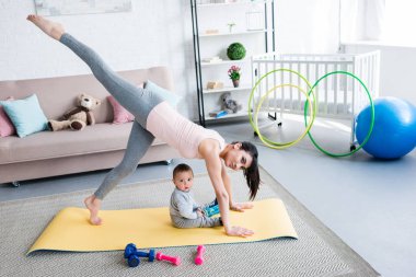 Genç Anne pratik yoga bir bacaklı aşağı doğru bakan köpek poz mindere evde oturan onun küçük bir çocuk iken