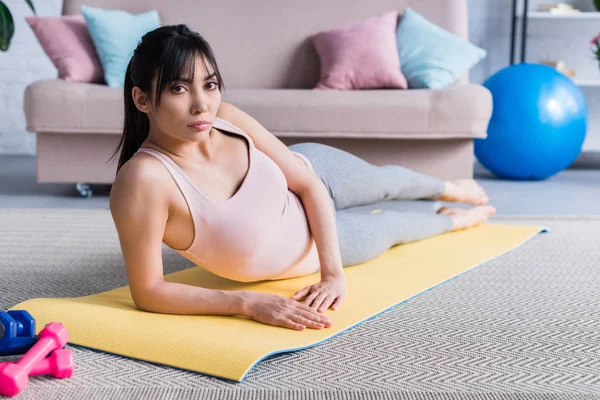 beautiful young woman lying on yoga mat at home and looking at camera