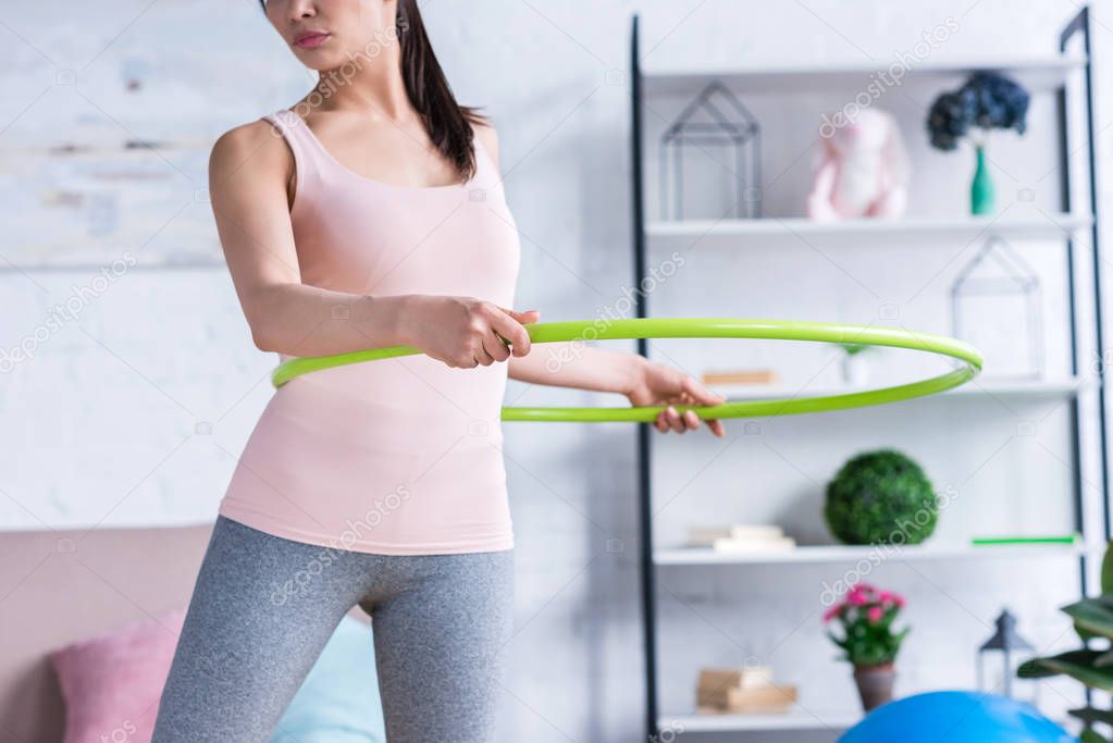 cropped shot of fit young woman working out with hula hoop at home