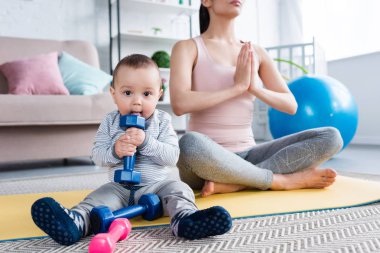 Genç Anne lotus poz evde dumbbell tutarak onun küçük bir çocuk iken meditasyon