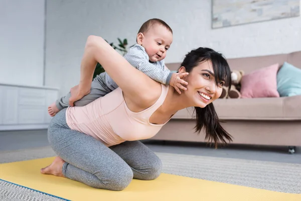 Kleines Kind Huckepack Auf Mutter Während Sie Hause Auf Yogamatte — Stockfoto