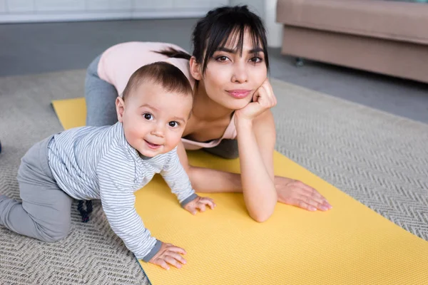 Ung Mamma Och Lilla Barnet Yogamattan Hemma Tittar Kameran — Stockfoto