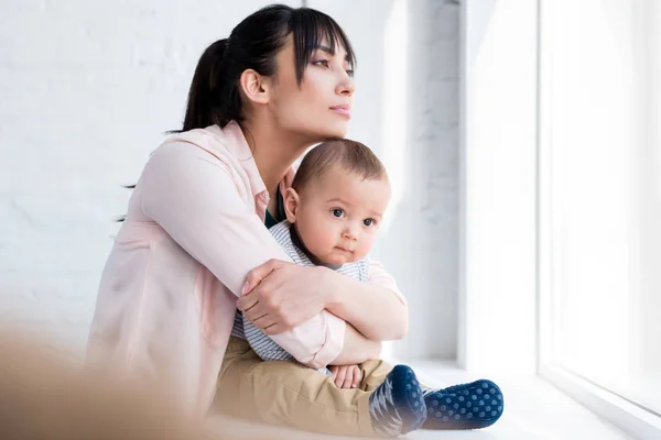 Young Beautiful Mother Embracing Her Little Child While Sitting Windowsill — Stock Photo, Image