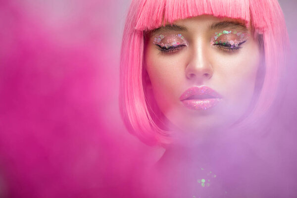 attractive woman with pink hair and makeup with glitter standing in pink smoke with closed eyes