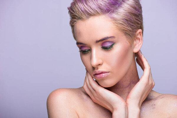 привлекательная женщина с фиолетовым блеском на шее и короткими волосами, смотрящая вниз изолированы на фиолетовый
