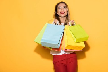 happy female shopper standing with paper bags on yellow background 