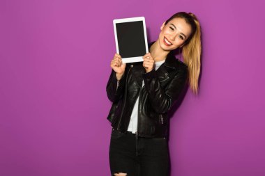 Dijital tablet tutarak ve violet izole kamera gülümseyen güzel genç kadın