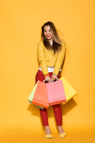 smiling asian woman with shopping bags on yellow background 