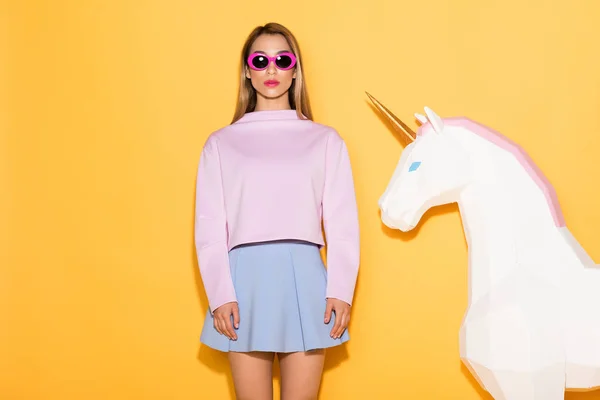 asian female model in sunglasses and decorative unicorn on yellow background