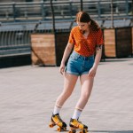 Menina bonita em calções jeans patinação rolo na rua