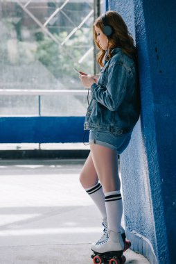kulaklıklar, denim giyim, yüksek çorap ve smartphone kullanarak paten şık kadın yan görünüm