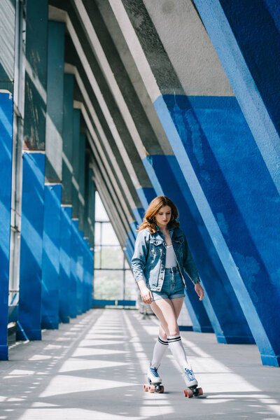 fashionable young woman in denim clothing and high socks roller skating alone