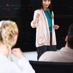 Asiático mujer de negocios mostrando presentación y apuntando a mujer colega en moderno oficina