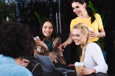 dizüstü ekran üzerinde modern ofisindeki iki iş kadınları gösteren gülümseyen iş kadını 