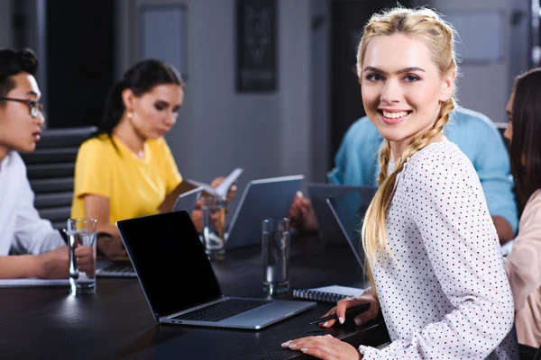 Sonriente Joven Empresaria Mirando Cámara Mientras Sus Colegas Trabajan Detrás — Foto de Stock