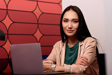 Genç Asyalı işkadını masada laptop ile modern ofisinde oturuyor. 