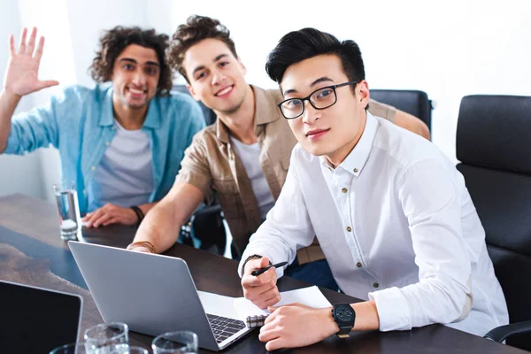 three multicultural businessmen at table with laptops in modern office