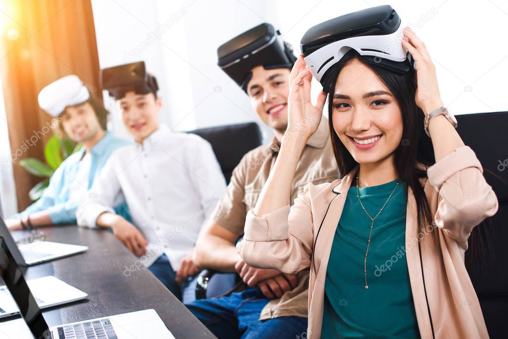 multiethnic business partners with virtual reality headsets at table with laptops in modern office 
