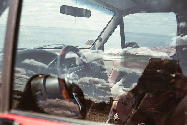 отражение облачного неба в окне автомобиля и моря позади
