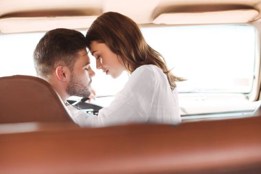 beautiful couple with closed eyes going to kiss in car together clipart