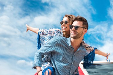 happy man piggybacking his smiling girlfriend with blue sky on background clipart