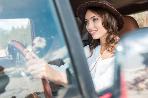 愉快的美丽的年轻妇女在帽子驾驶汽车在旅途中 — 图库照片