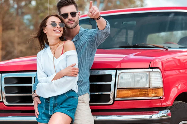 Smiling Man Hugging His Girlfriend Pointing Somewhere While Standing Red — Stock Photo, Image