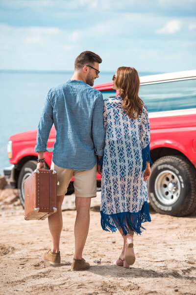back view of couple with suitcase going to red car